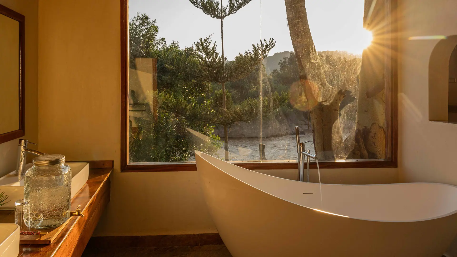 A freestanding bath beside a window looking out into the trees